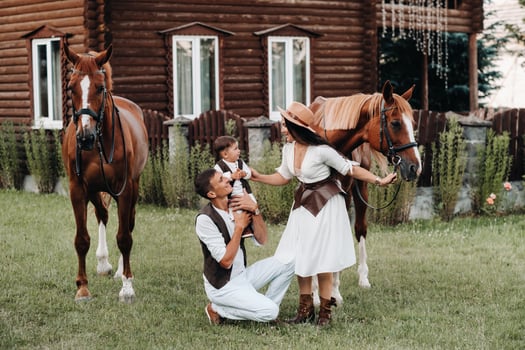 A family in white clothes with their son stand near two beautiful horses in nature. A stylish couple with a child are photographed with horses photo