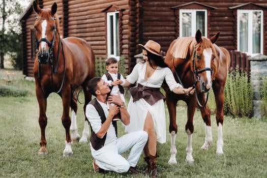 A family in white clothes with their son stand near two beautiful horses in nature. A stylish couple with a child are photographed with horses photo