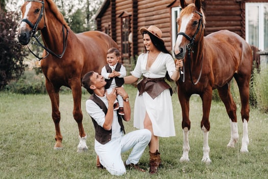 A family in white clothes with their son stand near two beautiful horses in nature. A stylish couple with a child are photographed with horses photo