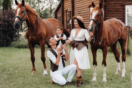 A family in white clothes with their son stand near two beautiful horses in nature. A stylish couple with a child are photographed with horses photo