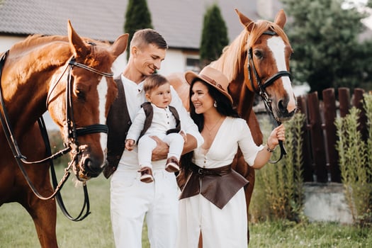 A family in white clothes with their son stand near two beautiful horses in nature. A stylish couple with a child are photographed with horses photo