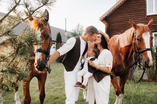A family in white clothes with their son stand near two beautiful horses in nature. A stylish couple with a child are photographed with horses photo