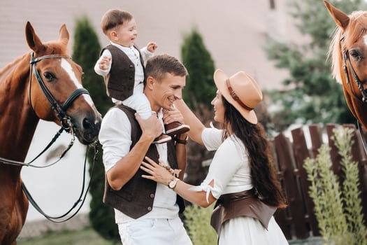 A family in white clothes with their son stand near two beautiful horses in nature. A stylish couple with a child are photographed with horses photo