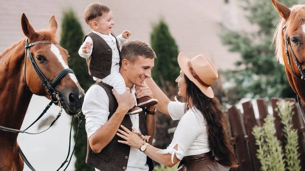 A family in white clothes with their son stand near two beautiful horses in nature. A stylish couple with a child are photographed with horses photo