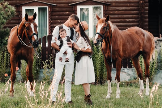 A family in white clothes with their son stand near two beautiful horses in nature. A stylish couple with a child are photographed with horses photo