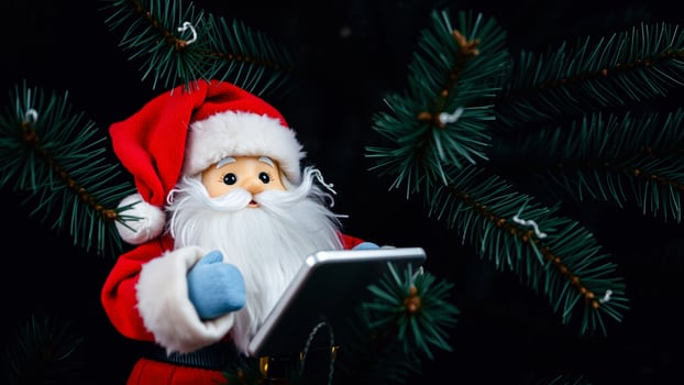 Santa Claus Using a Tablet in Front of a Christmas Tree photo