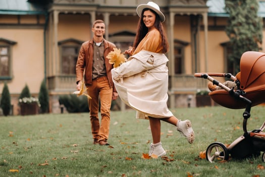Father and mother on a walk with a child in a stroller in the autumn Park on the background of the estate. A family walks through the Golden autumn nature Park photo