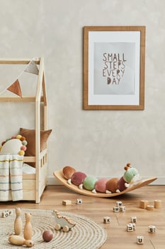 Stylish composition of cozy scandi child's room interior with mock up poster frame, bed, plush caterpillar on balance board, toys and hanging decorations. Creative wall, carpet on the floor. Template. photo