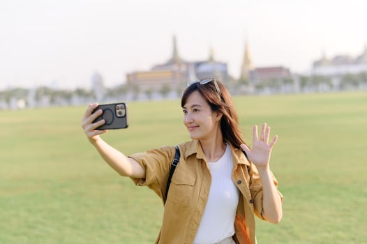 Traveler asian woman in her 30s making a livestream or selfie on smartphone while explores Wat Phra Kaew emerald Buddha. Share the wonders of Thai heritage through her journey. photo
