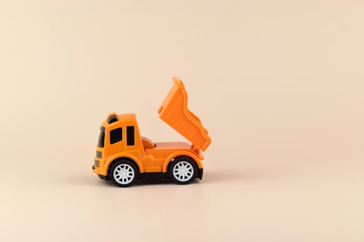Small orange toy truck on texture background of light color paper in minimal concept photo