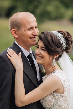 A man and woman are smiling at the camera. The man is wearing a black suit and the woman is wearing a white dress photo