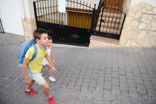 Two children walking together with backpacks on a cobblestone street photo