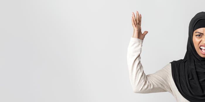 Angry black muslim girl in headscarf shouting and raising hands in fury and looking at camera, posing over light background photo