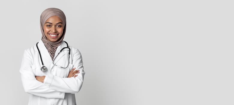 Medical Services For Muslim Women. Portrait Of Black Female Doctor In Hijab And White Coat Standing With Folded Arms Over Light Background In Studio. photo