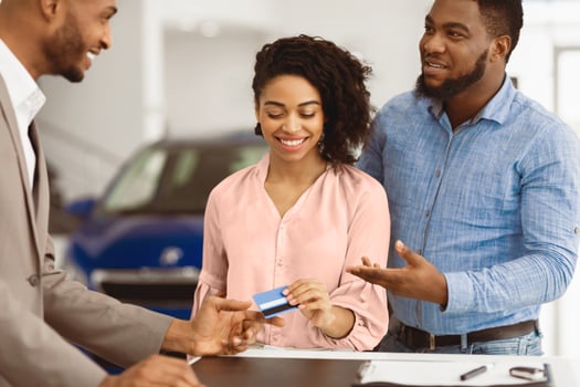 Car Purchase. African Couple Buying A Car Giving Credit Card To Auto Salesman In Dealership Office. Selective Focus photo