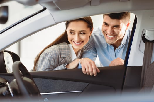 Taking A Closer Look. Beautiful smiling couple examining car before buying at the dealership, view from the inside photo