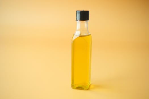 A Clear Glass Bottle filled with Cooking Oil set against a Bright Yellow Background photo