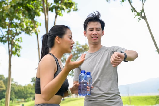 A healthy Asian couple resting after jogging together in a green park, drinking water. photo