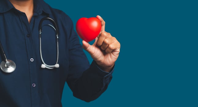 Hand of a doctor holding a red heart shape while standing on a blue background. photo