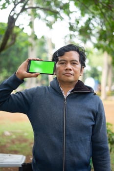Southeast Asian man showing something on his smartphone with a green screen, perfect for customizable content photo