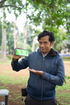Southeast Asian man showing something on his smartphone with a green screen, perfect for customizable content photo