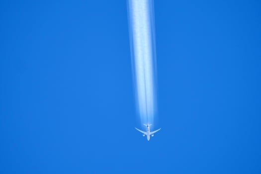 Airplane Flying High in Clear Blue Sky with Contrail Streaking Behind on a Sunny Day photo