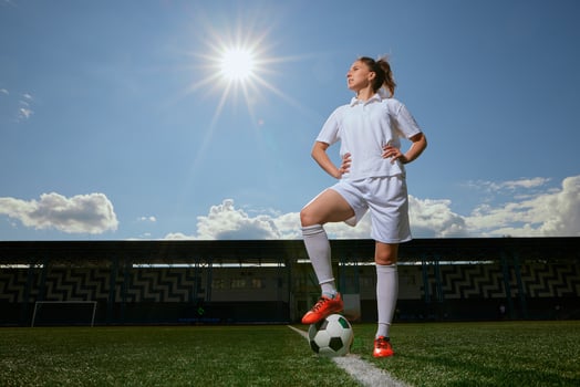 girl Football player in white shorts and red boots sets a soccer ball on a green field photo