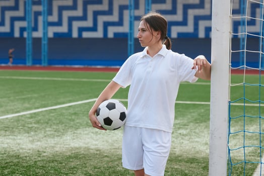 A female soccer player holds a soccer ball and leans against a goal post on a soccer field. photo