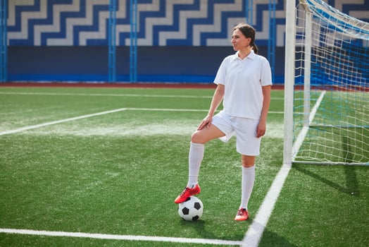 girl Football player in white shorts and red boots sets a soccer ball on a green field photo