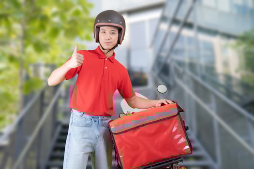 Cheerful young delivery man stands casually beside a red motorcycle photo