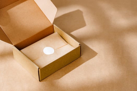 A sealed kraft box containing a wrapped item, positioned on a textured brown surface for an unboxing experience photo