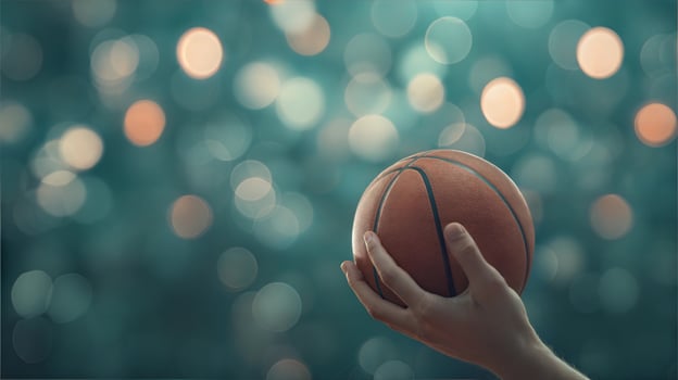A hand holding a basketball ball in front of a blurry background photo