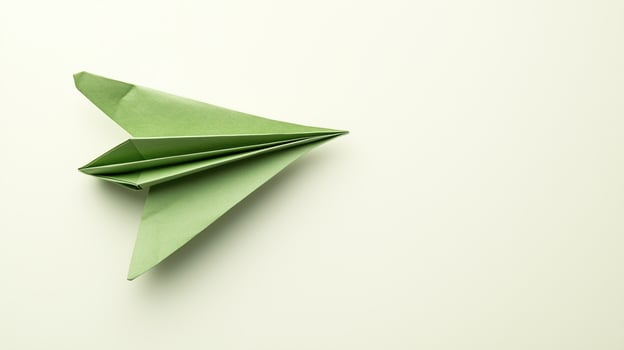 A top-down view of a verdant paper aircraft on a light backdrop photo