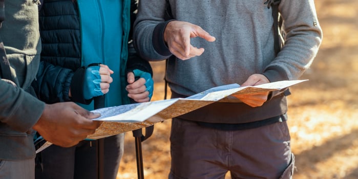 Cropped of multiracial friends with backpacks looking at map, hiking in autumn forest photo