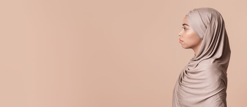 Profile portrait of black muslim woman in hijab looking at copy space over yellow background with serious face expression, side view photo