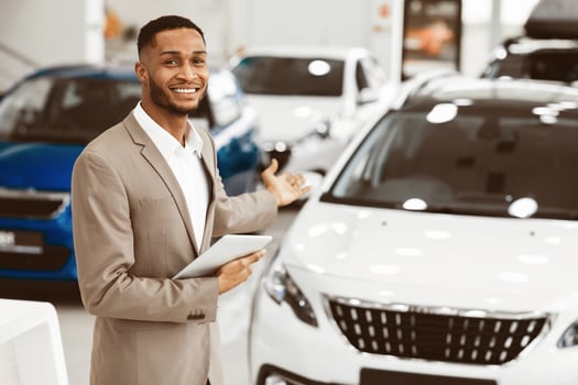Cheerful Car Dealer Gesturing Showing Brand-New Automobile Standing In Delarship During Luxury Auto Exhibition. Empty Space photo