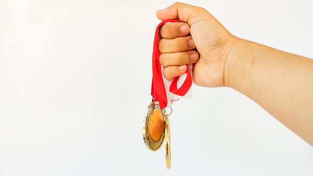 The winner's gold medal is held in the athlete's raised hand on a white background photo
