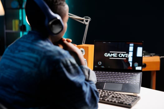 Black woman sitting and looking at her laptop screen displaying game over. Over the shoulder shot of african american female gamer gazing at personal computer after losing game. photo