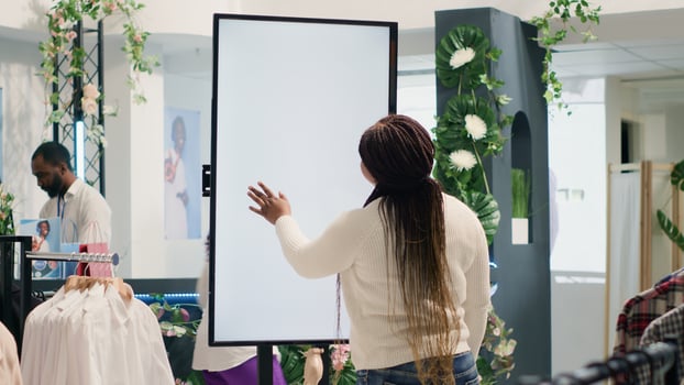 Customer in high tech thrift shop using digital isolated screen to find ideal outfit. BIPOC client in cheap second hand clothing store doing shopping using augmented reality kiosk photo