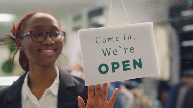 African american worker opening stylish fashion boutique, starting her shift in the morning. Employee turning closed sign on fast fashion clothing store into open one, close up shot photo