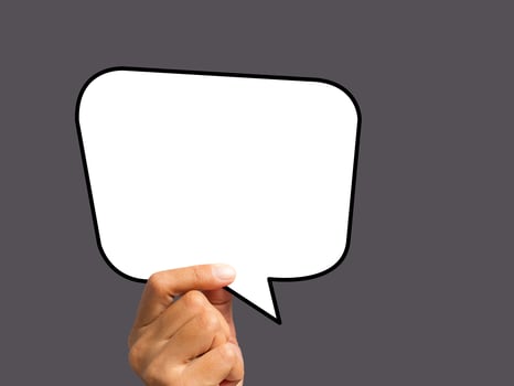 Hand holding of an empty white speech bubble against a gray background photo