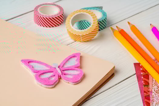 Colorful stationery arrangement with a butterfly sticker on a blank notebook at a wooden table in natural light photo