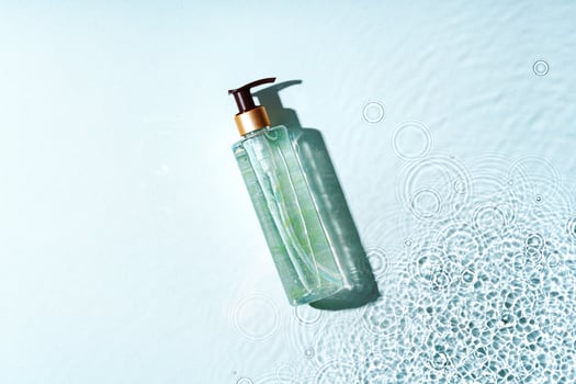 Clear bottle of gel product resting on a light blue surface with water droplets photo