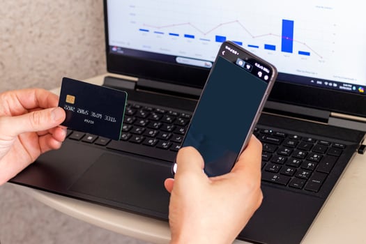 Shot of the man in the front of the laptop screen, holding credit card and the phone. Technology photo