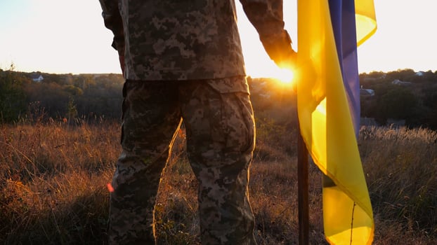 Male ukrainian army soldier stands with national banner against background of beautiful sunset. Young man in camouflage uniform with Ukraine flag as symbol of victory against russian aggression photo