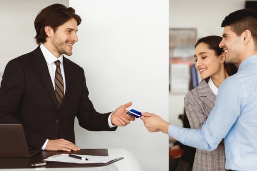 Happy Spouses Buying Car Giving Seller Credit Card Standing In Auto Dealership Office. Empty Space. Side View photo
