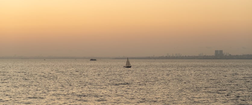 A lone sailboat gliding across the tranquil waters at sunset, with a soft orange sky in the background photo