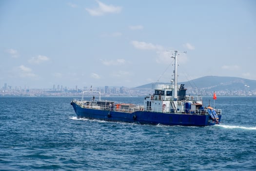 A blue cargo ship navigates the calm waters near a bustling city skyline on a clear day photo
