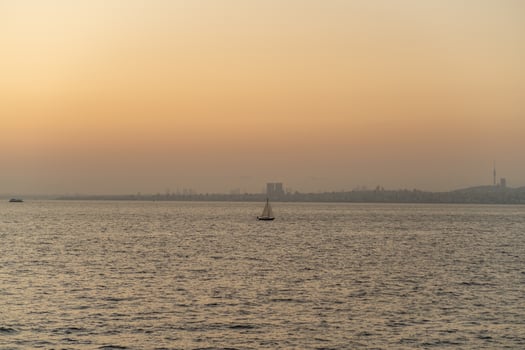 Sailing at dusk with a lone sailboat on tranquil waters near a city skyline during sunset photo