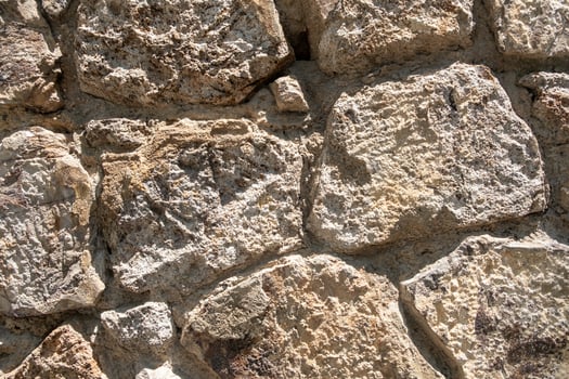 Close-up view of weathered stone wall featuring uneven textures and natural colors in sunlight photo